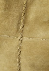 Zijden stof in een zachte gele tint, met een gevlochten naaddetail langs het midden en contrasterende stiksels voor extra textuur.