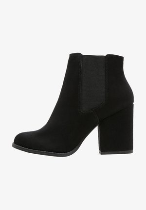 Bottines noires en daim avec un talon épais, des panneaux latéraux élastiques et un bout arrondi. Texture lisse avec des accents cousus le long de la semelle.