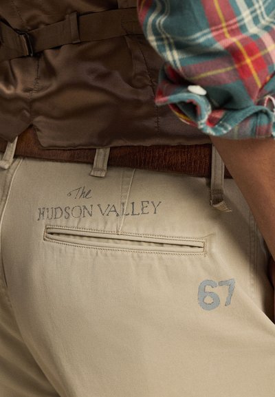 Khakibukser har en baklomme med et åpent spjeld og trykt tekst "The Hudson Valley" over lommen, med nummeret "67" under.