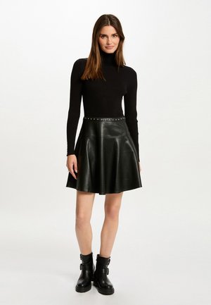Black ribbed turtleneck top paired with a high-waisted black leather flared skirt featuring silver studs along the waistband. Black ankle boots.