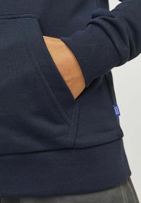 Felpa blu navy con polsini e orlo a costine, tasca ampia e tessuto testurizzato. Piccola etichetta blu sul lato.