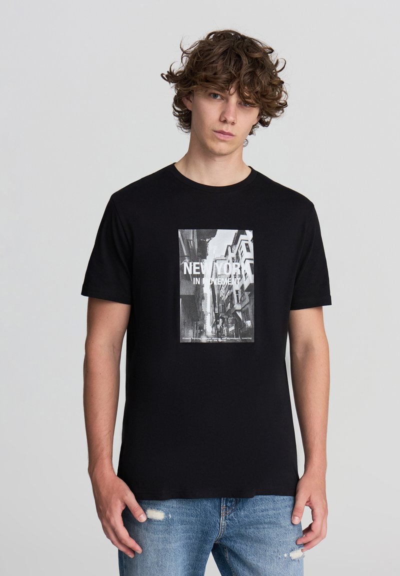 T-shirt in cotone nero con stampa grafica di una scena di strada in bianco e nero di New York, accompagnata da jeans chiari usurati.