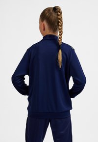 Marinblå sporttröja med långa ärmar, strukturerat tyg och hög krage. Har en söm baktill och subtila detaljer på axlarna.