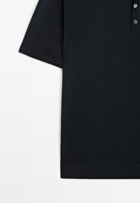 Polo nero a maniche corte, realizzato in tessuto testurizzato, con una chiusura a tre bottoni e un orlo a costine.