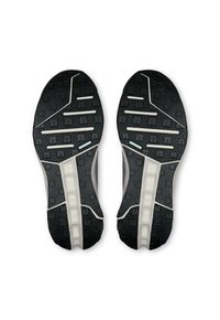 Suelas de zapatos de goma negra con un patrón texturizado, que presenta ranuras y crestas. Media suela de color gris claro acentuada con detalles en blanco.