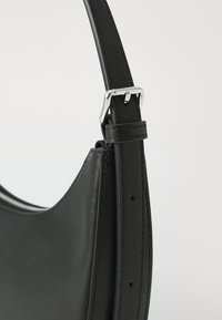Borsa a tracolla in pelle nera con una texture liscia, forma curva e tracolla regolabile, caratterizzata da hardware in tonalità argento e dettagli di cucitura.