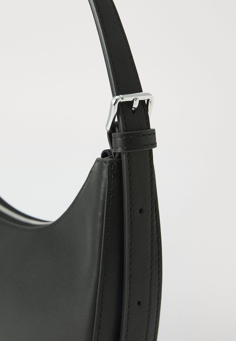 Czarna skórzana torebka o gładkiej fakturze, zakrzywionym kształcie i regulowanym pasku z metalowymi detalami w kolorze srebrnym oraz przeszyciami.