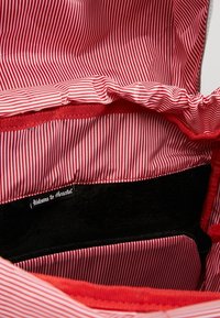 Tissu à rayures rouges et blanches à l'intérieur d'un sac avec une poche intérieure noire étiquetée "Bienvenue chez Herschel."
