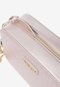Roze neplederen tas met een gestructureerd oppervlak, gouden hardware, bovenste ritssluiting en een geknoopte detail aan de ritssluiting.