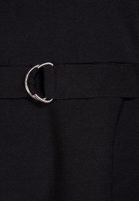 Un tissu noir avec une texture c�ôtelée présente une bande horizontale avec un détail en anneau métallique, solidement cousue à la taille.