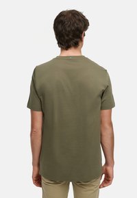 Camiseta de manga corta color verde oliva con cuello redondo, confeccionada en suave material de algodón, que presenta un pequeño detalle de logo en la parte trasera.