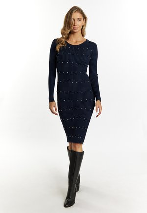 Marineblauw geribd gebreid jurk met lange mouwen, versierd met decoratieve witte kralen doorheen, aangevuld met een goed aansluitende silhouet en kniehoogte zwarte laarzen.