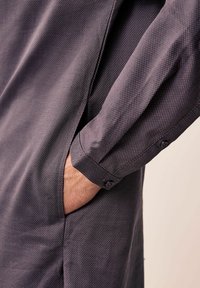 Siva košulja dugih rukava s teksturiranim uzorkom. Ima manžetne na drukanje i bočnu džep. Tkanina izgleda lagano i glatko.