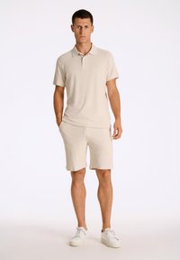 Beige pikétröja och matchande shorts i textureradt tyg. Outfiten har en klassisk krage och sidofickor, tillsammans med vita sneakers.