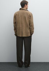 Brown suede jacket with a relaxed fit, button-up front, and shirt collar, paired with loose black trousers. No visible patterns.