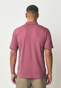 Polo tričko s krátkym rukávom v farbe prachovej ružovej, vybavené klasickým golierom, jemnou textúrou a zrolovanými manžetami, zobrazené zozadu.