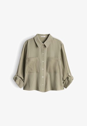 Camicia a maniche lunghe verde oliva chiaro con trama, bottoni frontali, due tasche sul petto e maniche arrotolabili fissate con patte con bottone.