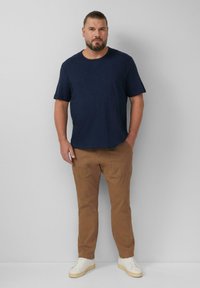 Marineblauw T-shirt met korte mouwen, casual pasvorm, gecombineerd met khaki slim-fit broek. Lichtgekleurde schoenen maken de outfit compleet. Effen achtergrond.