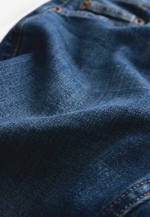 Denimová tkanina v tmavě modré barvě se hladkým povrchem. Obsahuje akcenty šití a mírně zmačkaný vzhled, který zdůrazňuje její měkkost.