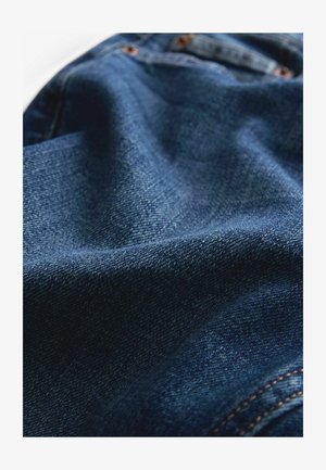Denimstof in donkerblauw met een gladde textuur. Heeft stiksels als accent en een licht gekreukelde uitstraling, wat de zachtheid benadrukt.