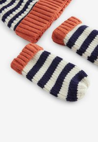 Ensemble bonnet et moufles en tricot rayé orange, marine et crème ; présente une texture côtelée et des bords retroussés. Tissu doux et chaud pour les temps froids.