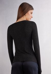 Sort langærmet top med rund halsudskæring, lavet af tekstureret stof med subtile glimmer accenter, tætsiddende design og en buet kant.