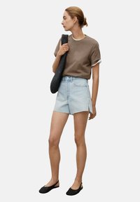 Rjav bombažni T-majica, svetlo modri jeans kratke hlače z bočnimi razporki, črna pletena torba in črne natikače. Preprost, vsakdanji outfit.