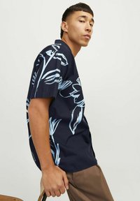 Camicia a maniche corte di un blu navy scuro con un grande motivo floreale azzurro, realizzata in un tessuto leggero. Presenta una vestibilità comoda e una chiusura con bottoni.