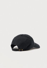 Zwarte verstelbare honkbalpet liggend op een lichte ondergrond, met zicht op de achterkant met metalen gesp en opening.