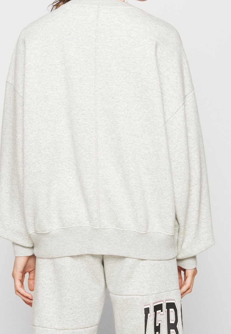 Felpa grigia con una vestibilità casual, tessuto morbido e spalle scese. Presenta un orlo a costine e cuciture pulite, abbinata a pantaloni coordinati.