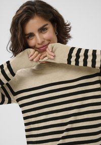 Beige sweater med markante sorte vandrette striber, ribbede ærmekanter og en afslappet pasform. Blød tekstur med lange ærmer og rund halsudskæring.