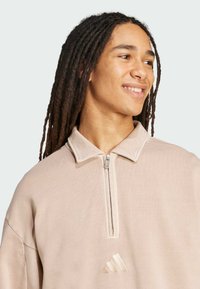 Beige kvartsg zip sweatshirt med en mjuk textur, med en krage och en broderad Adidas-logotyp på bröstet.