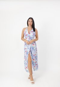 Robe maxi florale bleu clair avec des motifs rouges et roses, décolleté halter, design enveloppant et fente jusqu'à la cuisse.