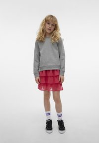 Grå sweatshirt, rosa lager av tylkjol, svarta sneakers med kardborreband och vita strumpor med lila ränder. Står på en vit bakgrund.