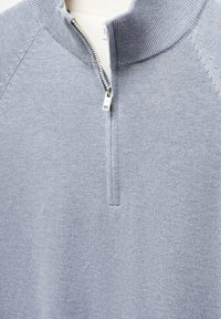 Hellblauer Pullover mit hohem Kragen und halbem Reißverschluss. Verfügt über gerippte Bündchen und Texturen. Hergestellt aus weichem, gestricktem Stoff.