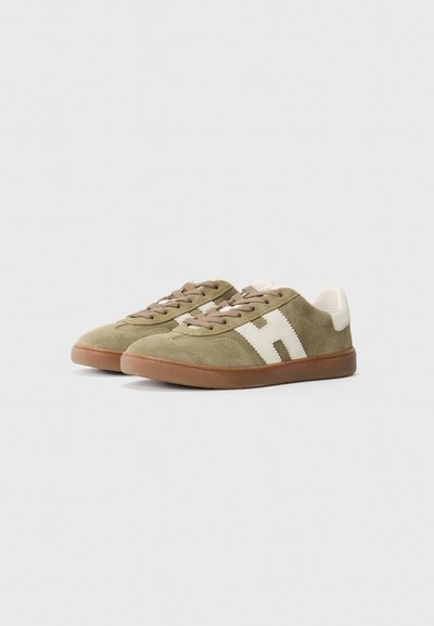 Een paar olijfgroene suède sneakers met witte "H" logo's aan de zijkanten, bruine veters en gumrubberen zolen op een witte achtergrond.