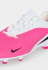 Λευκό και ροζ ποδοσφαιρικό παπούτσι Nike με μαύρο σύμβολο, διαμορφωμένες μύτες και λευκά κορδόνια σε απλό φόντο.