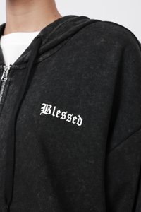 Svart hettegenser med glidelås laget av myk stoff. Har hvit "Blessed" tekst på brystet. Inkluderer foret hette og frontglidelås.