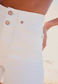 Weiße hochgeschnittene Jeans mit Kupferknopf-Details und Fronttaschen, ausgestattet mit einer glatten Textur und tailliertem Design.