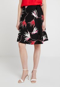 Gonna nera con motivo floreale in rosso, rosa e bianco. Presenta una vita aderente con un fiocco e una forma svasata, lunga fino al ginocchio.