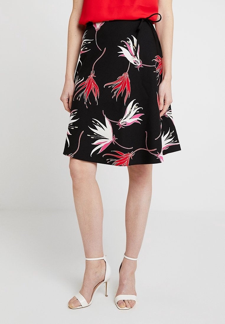 Gonna nera con motivo floreale in rosso, rosa e bianco. Presenta una vita aderente con un fiocco e una forma svasata, lunga fino al ginocchio.