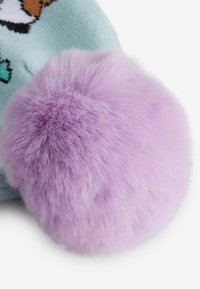 Vêtement bleu clair avec un pompon en peluche violet. Le pompon est rond, duveteux et doux, créant un contraste visuel avec la texture du vêtement.