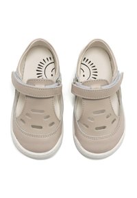 Zapatos de cuero beige claro con detalles troquelados y una correa de velcro. Suela de goma blanca. El interior presenta un gráfico del sol en el forro beige.