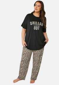 Mustat ylipitkät t-paidat, joissa on tekstit "CHILLED" ja "OUT", yhdistettynä vaaleanbeigeihin leopardikuosisiiin pyjamahousuihin. Pehmeä kangas, löysä istuvuus, rento malli.