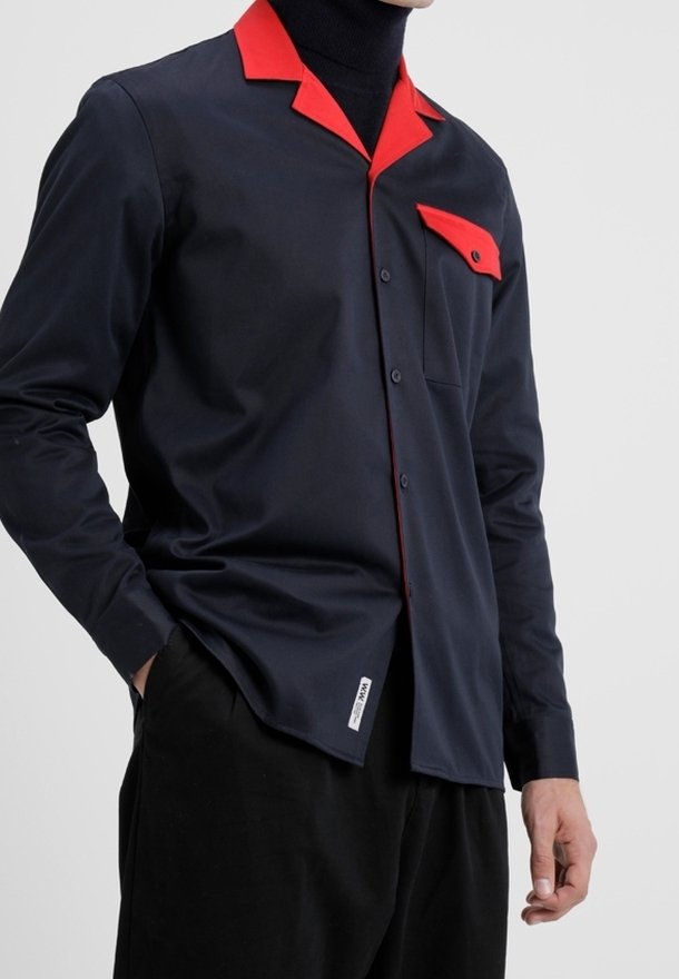 Mörkblå skjorta med knappar och röd krage och ficka. Har en slim fit, slät textur och sydda detaljer på fickan.