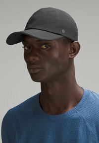 Schwarze Kappe aus glattem Stoff mit einem gebogenen Schirm. Auffälliges Logo-Akzent an der Seite. Getragen mit einem strukturierten blauen Sportshirt.