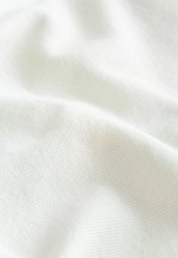 Tissu blanc doux avec de légers plis et une texture tissée fine, suggérant un matériau lisse et léger.