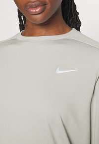 T-shirt de sport Nike gris clair avec un col rond, en tissu lisse, et un petit logo Nike blanc sur l'épaule gauche.