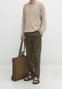 Top beige a maniche lunghe, pantaloni verde oliva, borsa a tracolla marrone, sandali marroni con cinturini, texture liscia, vestibilità comoda.