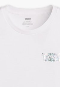Bela majica s kratkimi rokavi z bleščečim logotipom Levi's v svetlo modrem in srebrnem dizajnu. Narejena iz mehkega bombažnega materiala.